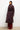 Person wearing a long dark coat and red pants against a white background
