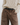Brown jeans worn with a beige cable knit sweater on a plain background